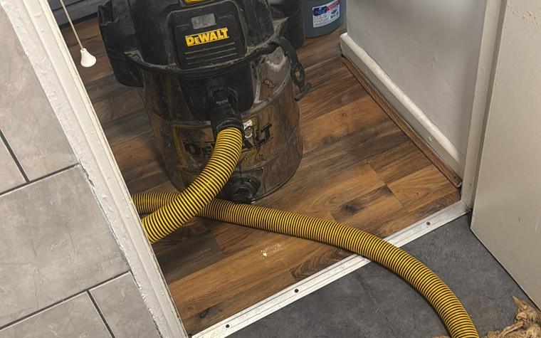 Wet vacuum and hose lifting standing water from a bathroom floor